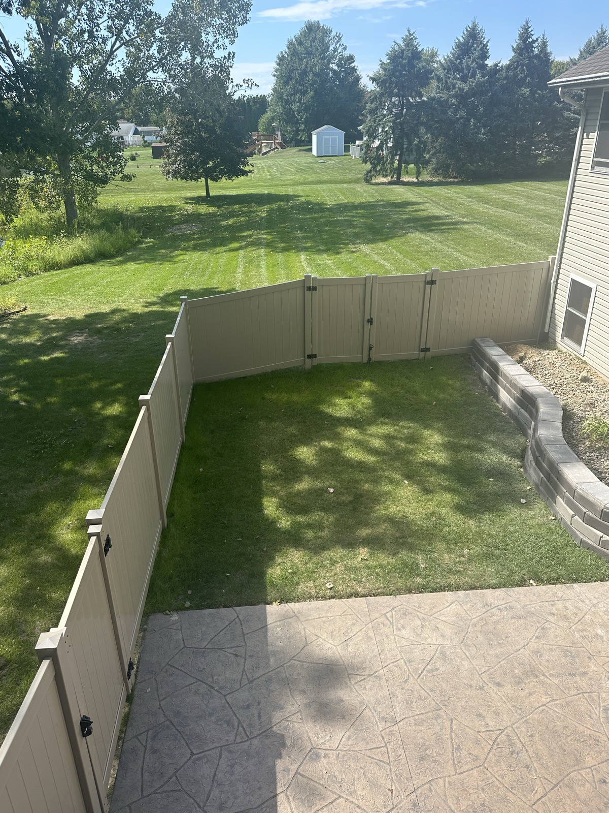 Tan vinyl privacy fence enclosing a backyard patio, seen from an upper window of a Northern Indiana home