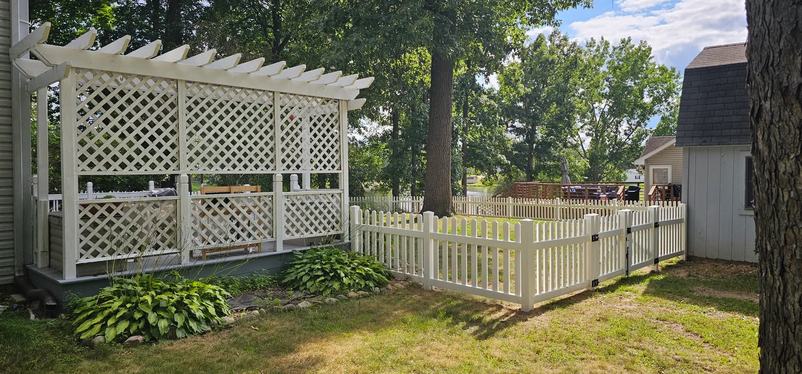 The same back yard after installation, enclosed by a white vinyl picket fence running from the pergola to the shed