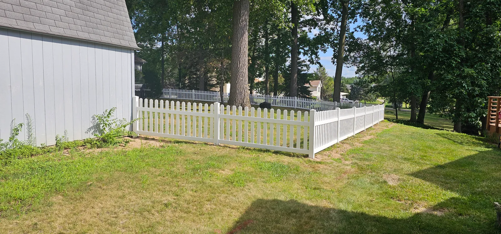 Picket fence line running along the side of the shed and down the property edge toward the street trees