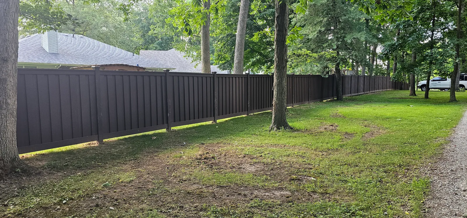 A long run of finished composite privacy fence curving through mature trees