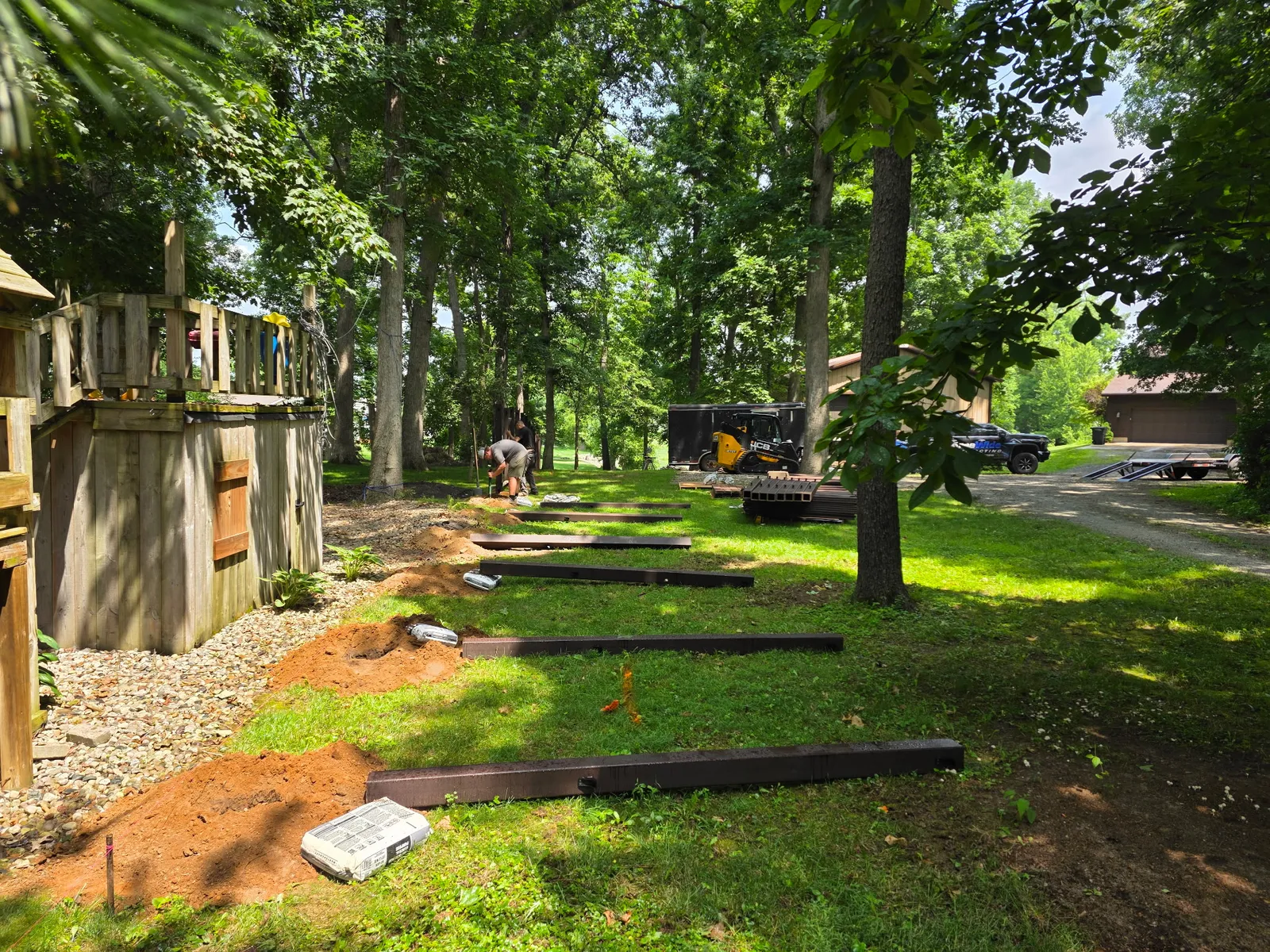 Freshly dug post holes along a wooded backyard fence line, ready for a new composite privacy fence
