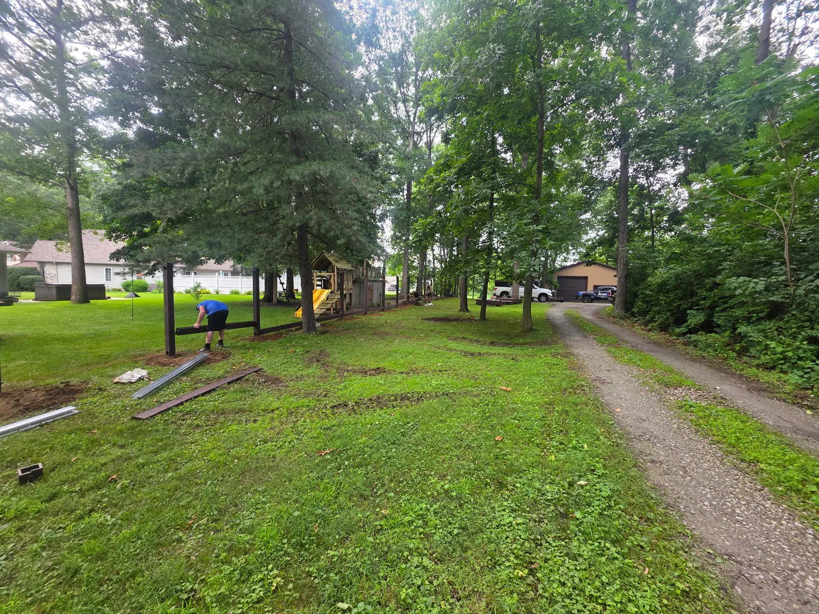 Composite fence posts set in a row through a wooded backyard, with a rail ready near a play structure