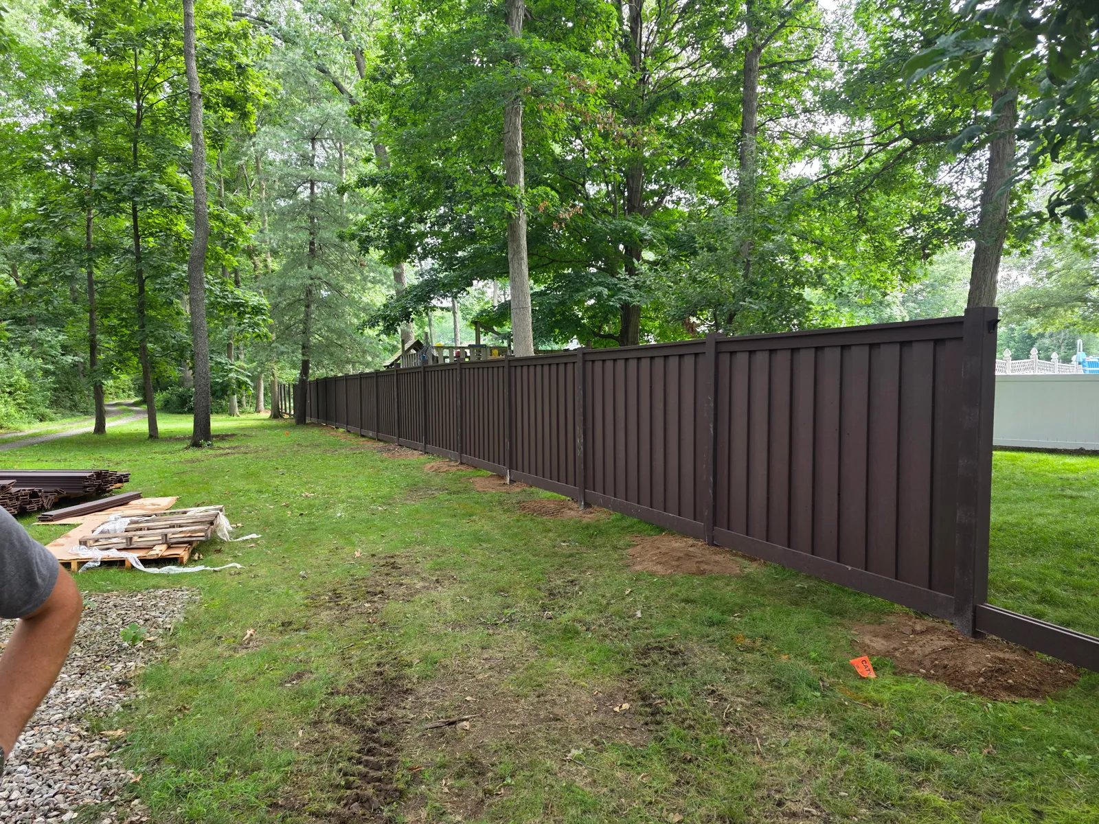 A finished stretch of dark brown composite privacy fence along a tree-lined property line