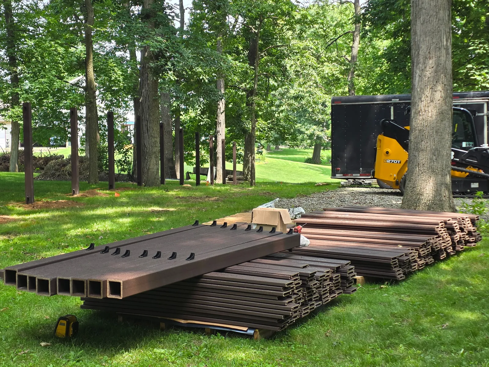 Stacks of brown composite fence boards and posts staged on the lawn before installation